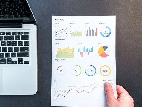 Frauenhand mit Statistiken, daneben ihr Laptop