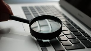 Eine Lupe streift über die Tastatur eines Laptops