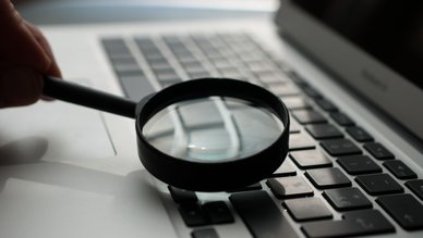 Eine Lupe streift über die Tastatur eines Laptops